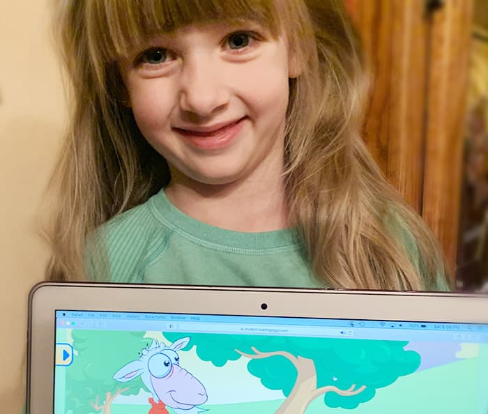 Smiling five year old girl with Reading Eggs online program on laptop.
